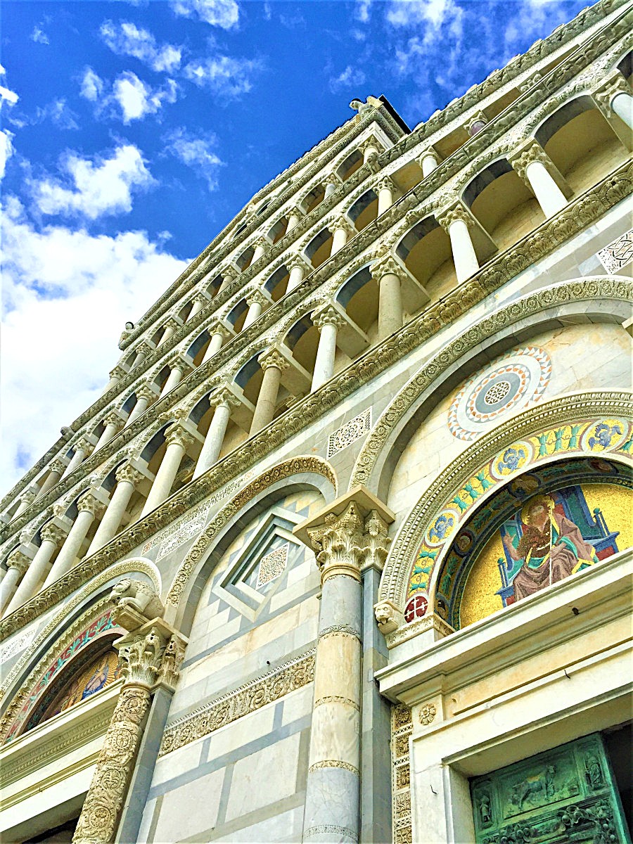 Close-up view of the Pisa Cathedral’s Romanesque marble facade with arches, columns, and mosaics against a bright blue sky in Piazza dei Miracoli.