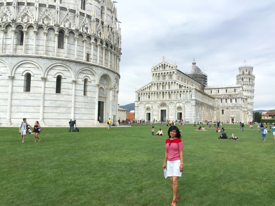 Traveler standing on the lawn at Piazza dei Miracoli in Pisa with the Baptistery, Cathedral, and Leaning Tower in the background after walking from Pisa Centrale.