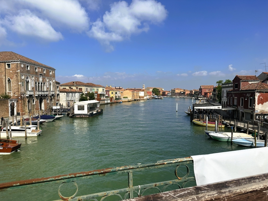 View of Murano’s main canal lined with colorful Venetian buildings and boats under a clear blue sky, seen upon arrival from Venice