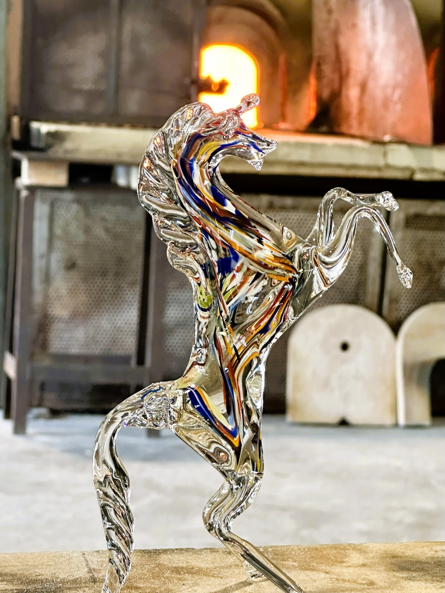 Close-up of a handcrafted Murano glass horse sculpture with vibrant colors, captured against the glowing furnace of a glass workshop in Murano, Italy