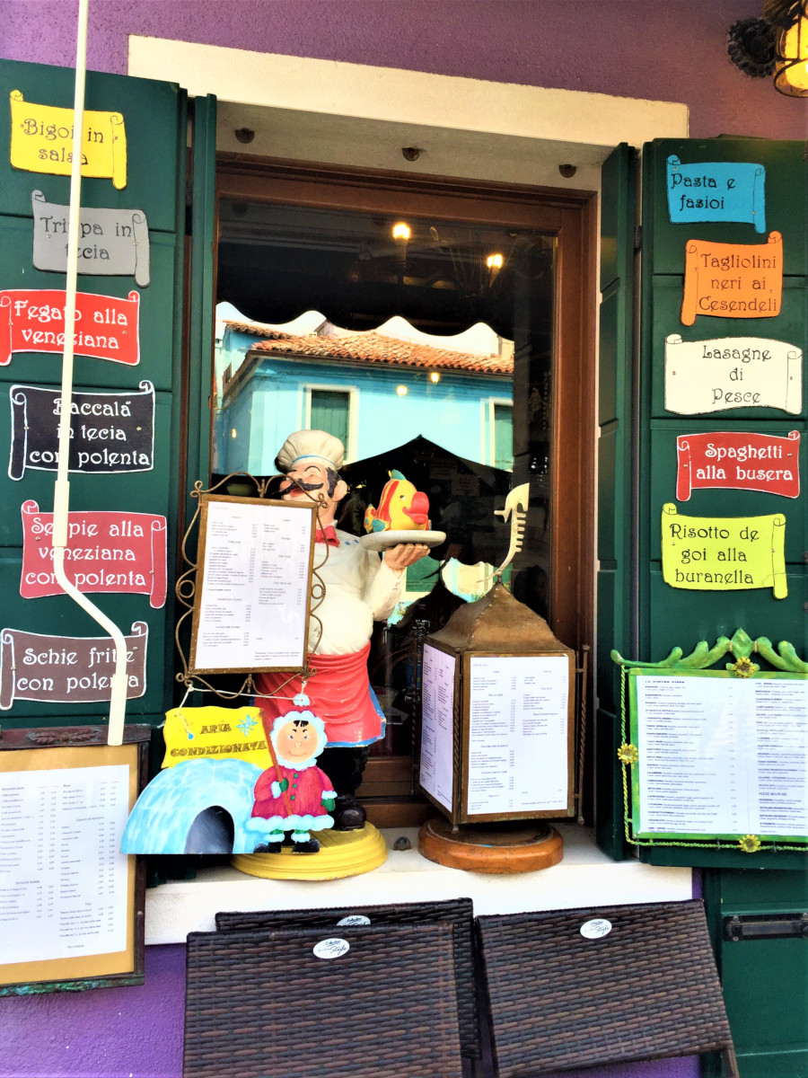 Colorful restaurant window and seafood menu in Burano, Italy with vibrant signs and local charm