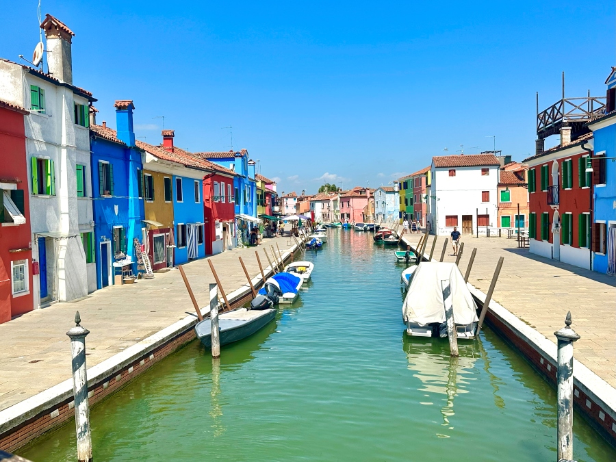 Colorful canal view in Burano, Italy — boats moored along vibrant houses under a bright blue sky