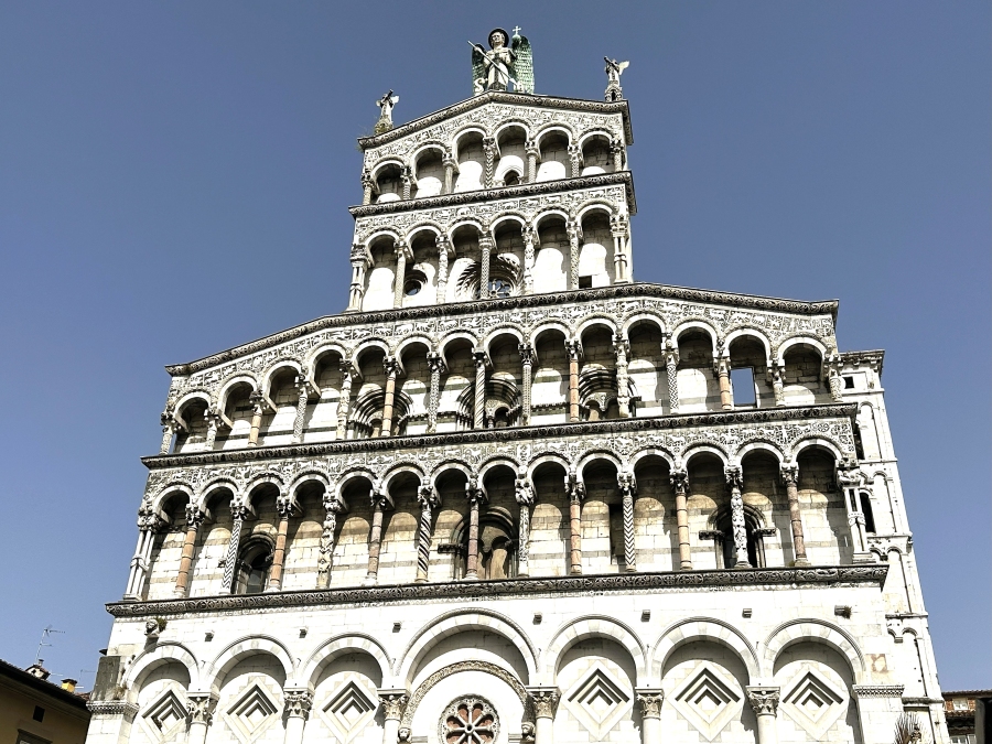 Façade of the Church of San Michele in Foro in Lucca, Italy, featuring Romanesque architecture and detailed marble carvings against a blue sky.