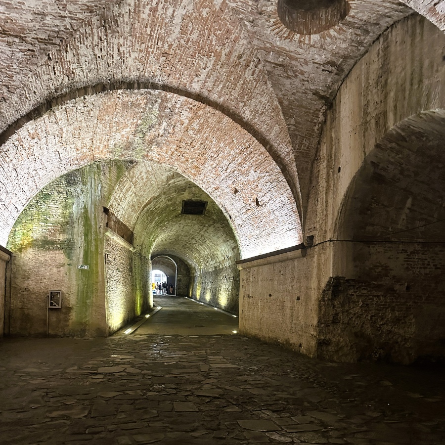Brick-arched tunnels beneath the historic walls of Lucca, Italy, illuminated by soft light and showcasing centuries-old architecture.