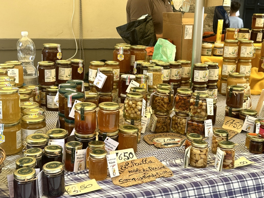 Display of locally sourced Tuscan products on Via Fillungo in Lucca, Italy — including olive oils, honey, and artisanal goods in glass jars.