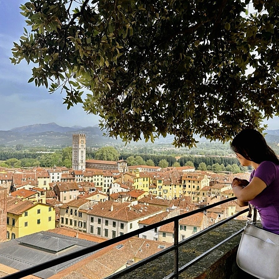 Woman admiring the panoramic view of Lucca’s terracotta rooftops and medieval towers from the Guinigi Tower in Tuscany, Italy