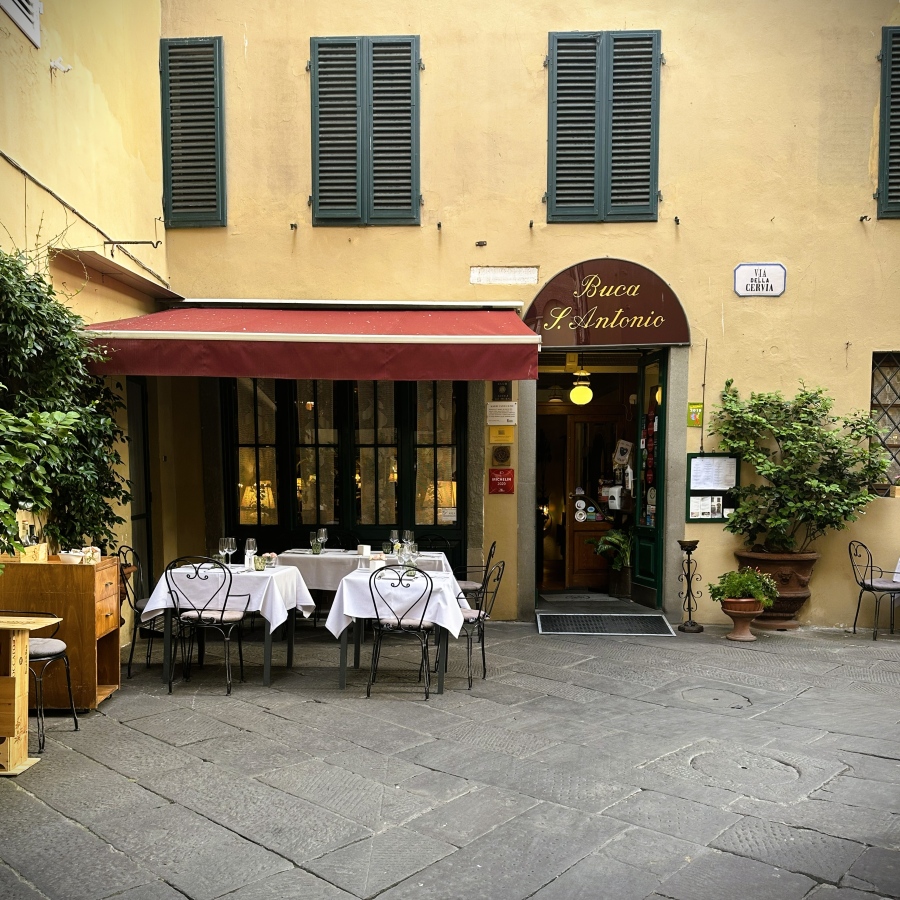 Exterior view of Ristorante Buca di Sant’Antonio in Lucca, Italy, with outdoor dining tables set under the restaurant’s yellow façade.