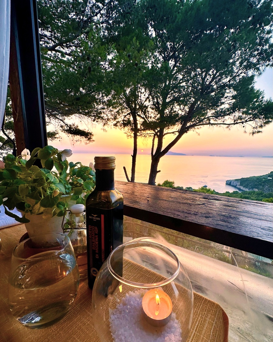 Sunset view from a dinner table at Da Emilia alla Curtiglia in Anacapri on Capri Island, with olive oil, a candle, and Mediterranean sea cliffs in the background.